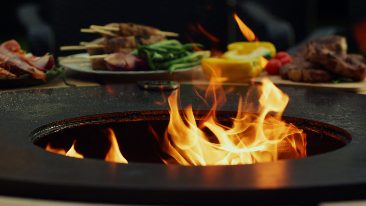 Flamara Feuerplatte mit offener Flamme in der Mitte, am Rand Spieße, Bohnen, Paprika und Steaks