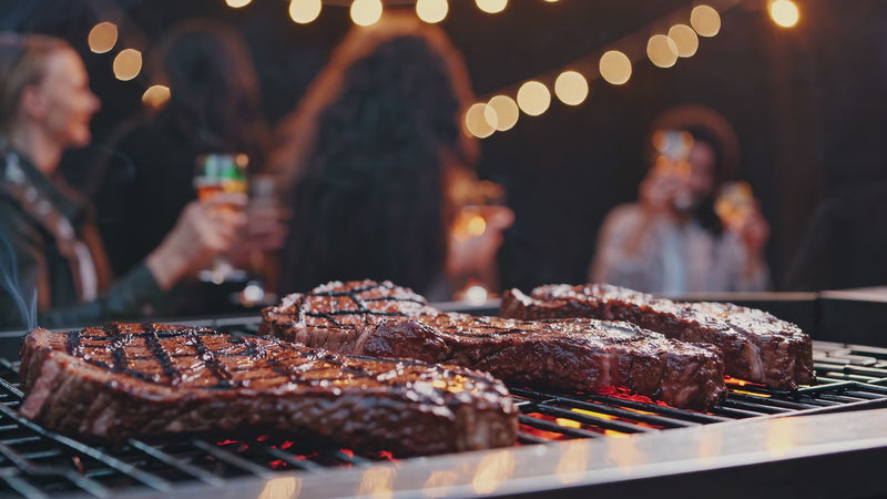 Steaks auf dem Grill, Gaeste mit Glaesern im Hintergrund