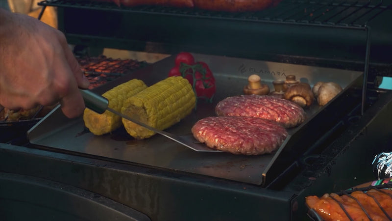 Burger, Maiskolben und Pilze auf der Flamara Plancha, Hand mit Grillwender
